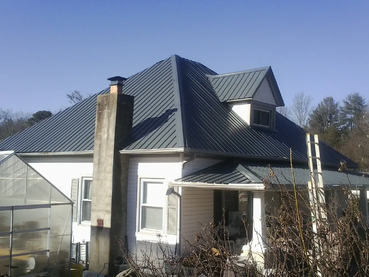 Dark blue standing seam metal roof on a white farmhouse with dormer — Slate & Tile Roof Repair by Roofing Brothers in Mount Freedom