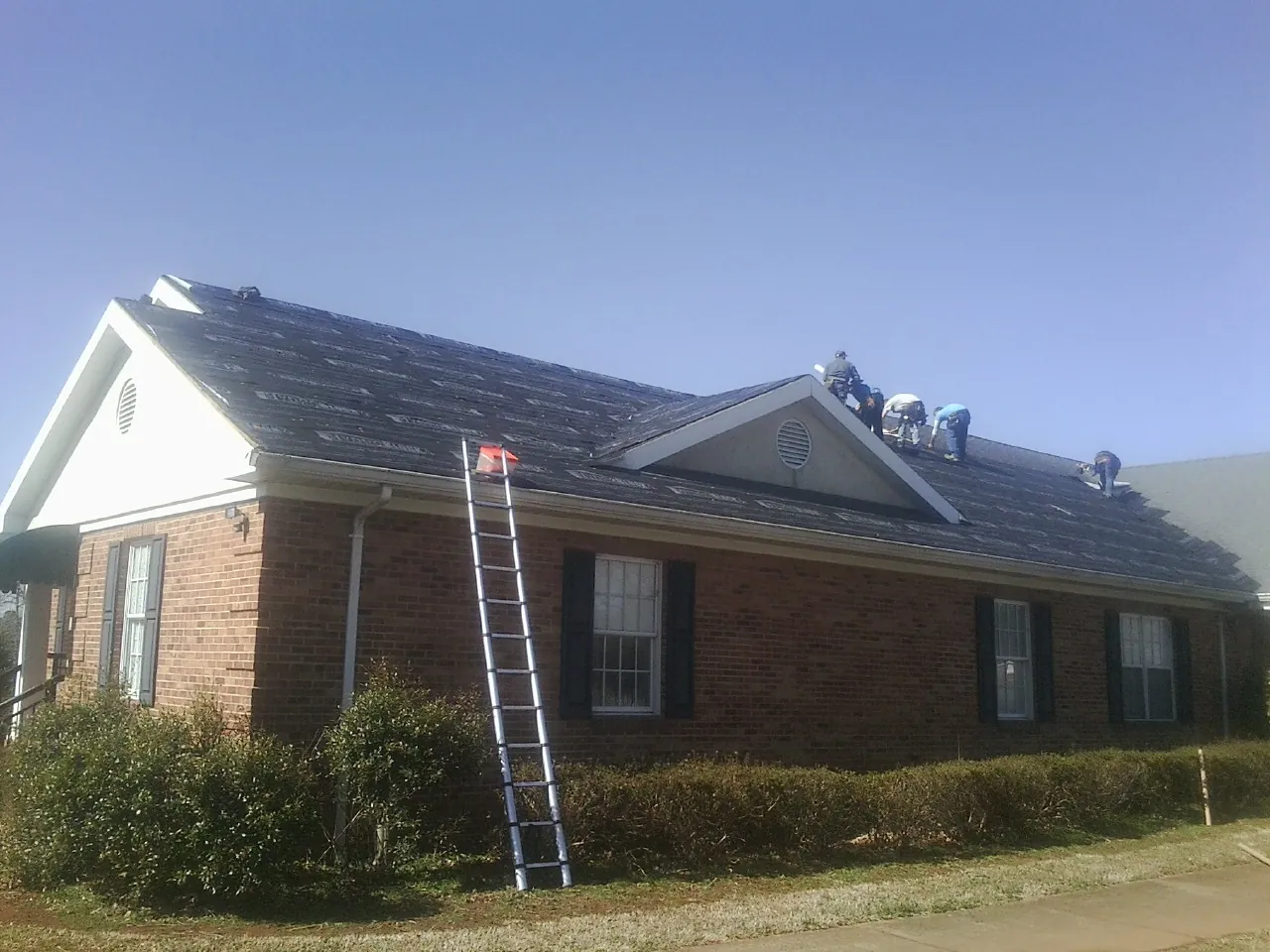 Crew tearing shingles off a brick ranch roof with a ladder set — Emergency Roof Repair work by our crew in Mount Freedom