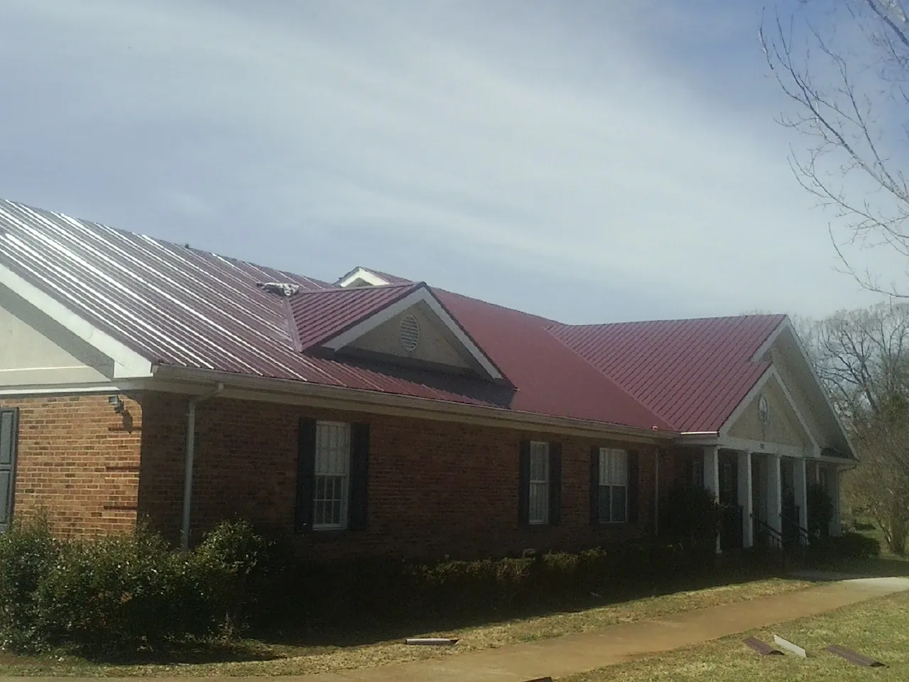 Red metal roof with gabled entries on a long brick building, from a Hail Damage Roof Repair job in Mount Freedom