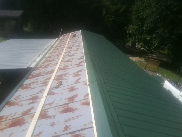 Old rusted panels beside newly installed green metal roofing — Wind Damage Roof Repair by Roofing Brothers in Mount Freedom