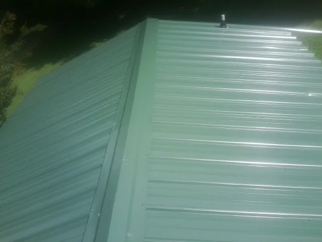 New green metal panels meeting at the ridge of a roof — Flat Roof Repair work by our crew in Mount Freedom