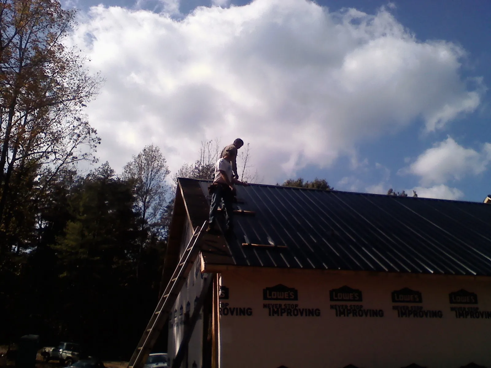 Roofer fastening dark metal panels high against a cloudy sky, from a Roof Inspection job in Mount Freedom