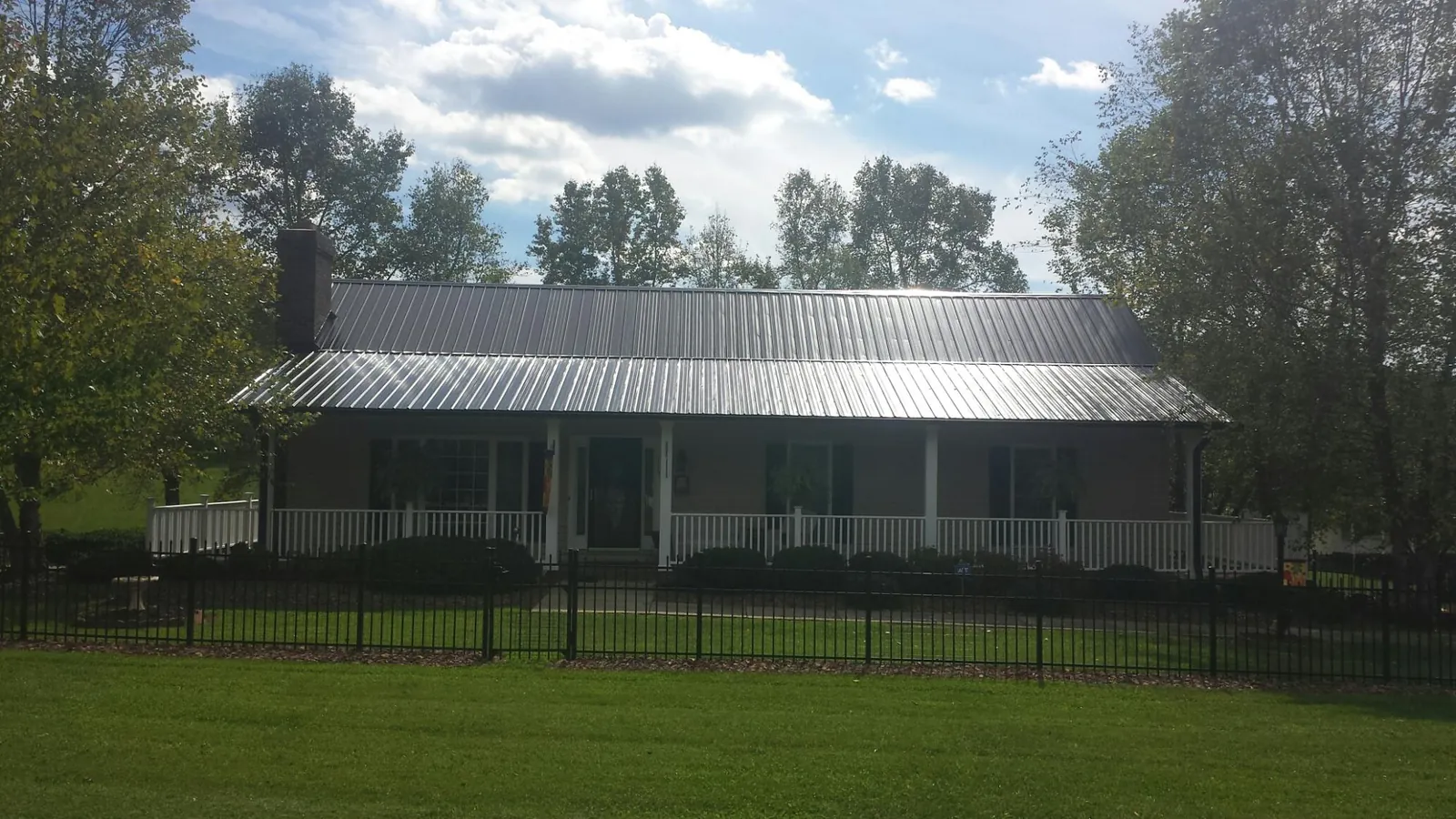 Gray metal roof on a brick ranch with a full width front porch — Gutter Guard Installation work by our crew in Mount Freedom