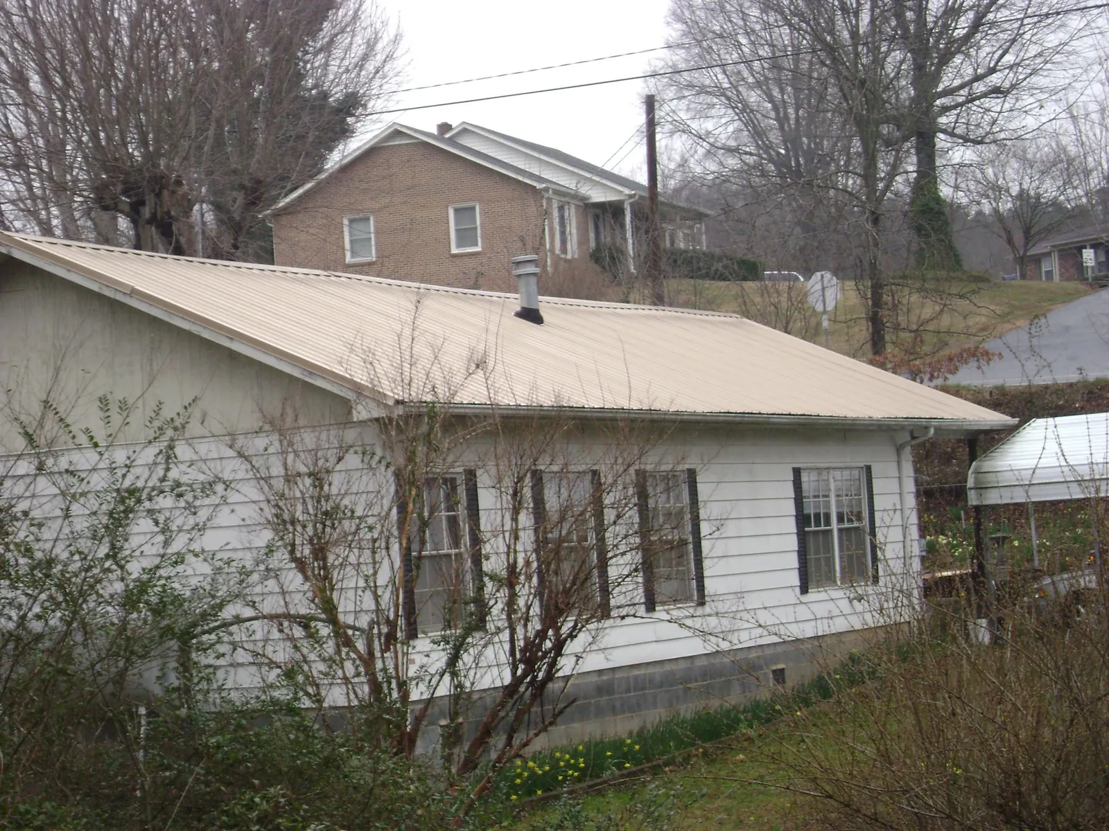 Tan metal roof on a white sided house set into a hillside — Commercial Roofing by Roofing Brothers in Mount Freedom