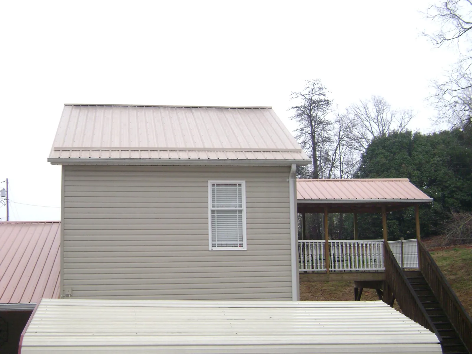 Tan metal roofs on a two story addition and attached porch, from a Roof Replacement job in Mount Freedom